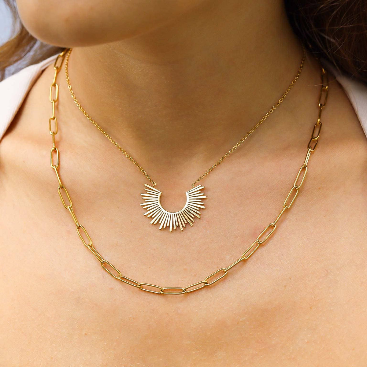 Gold chain necklace with a sunburst pendant on a person's neck