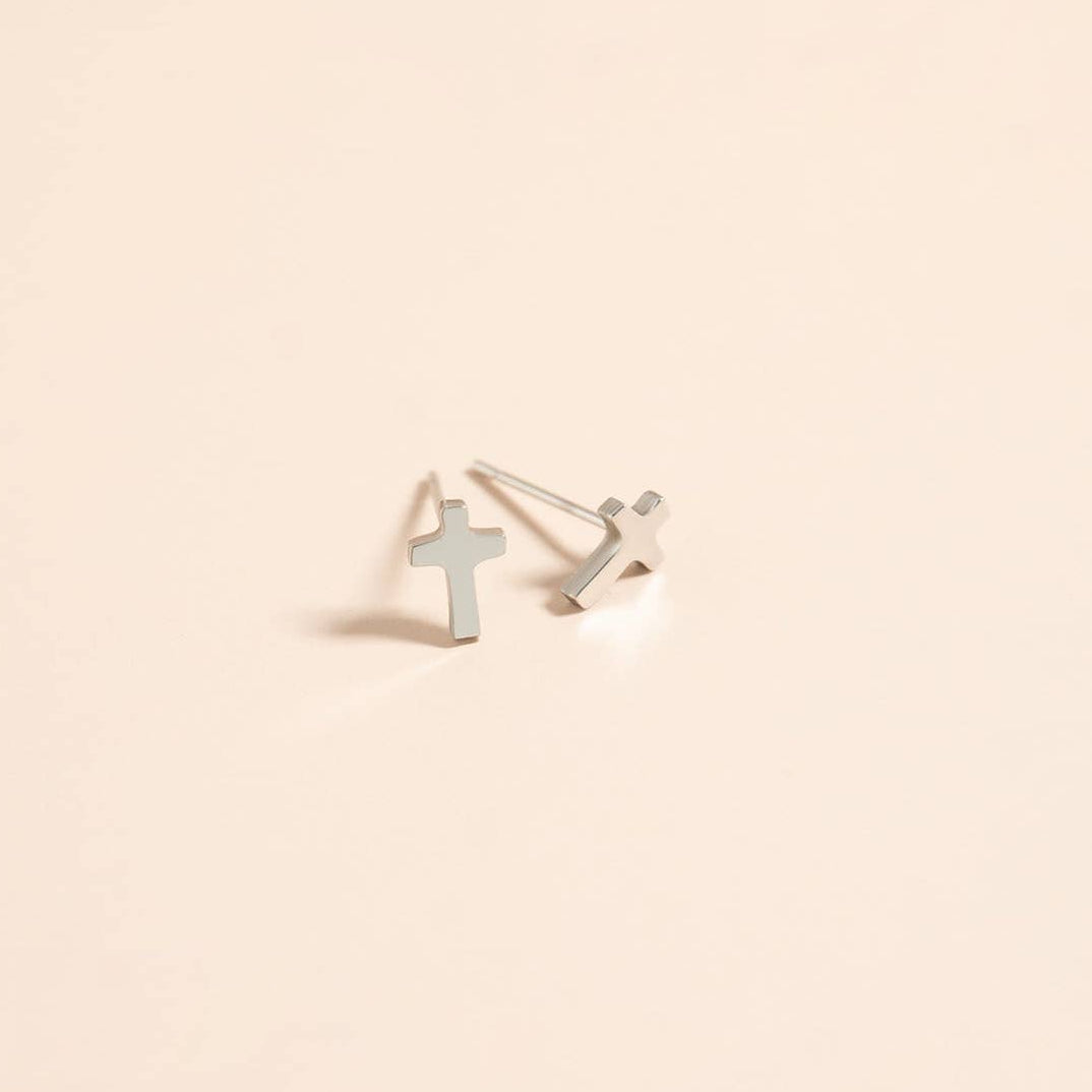 Silver cross-shaped earrings on a beige background
