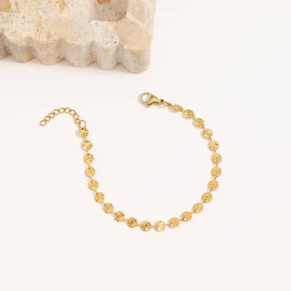 Gold bracelet on a white background with a textured beige object in the corner.