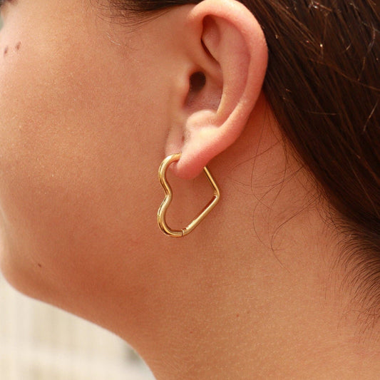 Close-up of a person wearing a gold heart-shaped hoop earring.