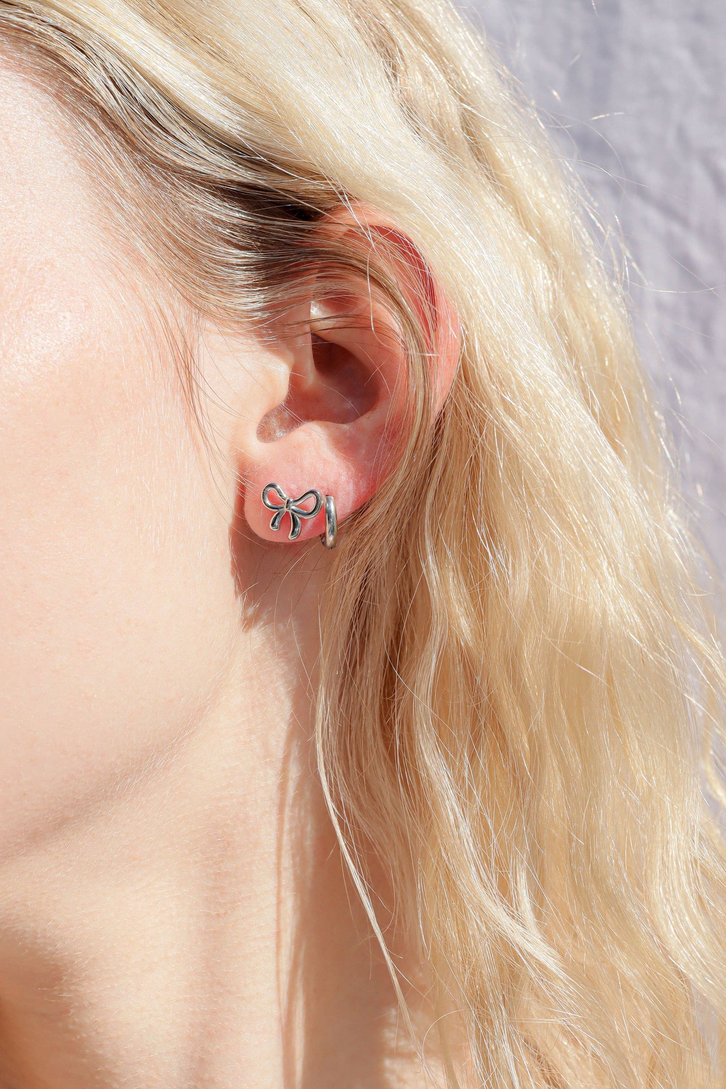Close-up of an ear wearing a bow-shaped earring with blonde hair and a neutral background