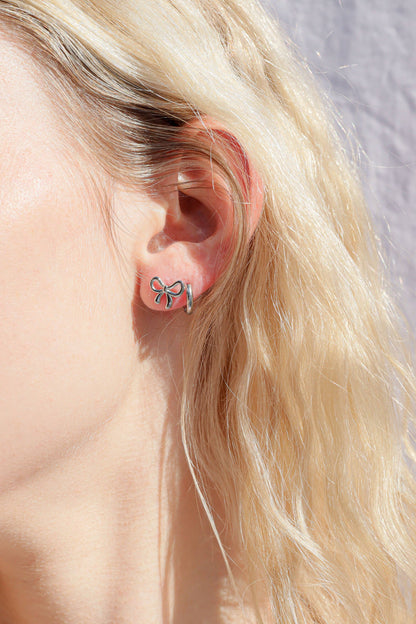 Close-up of an ear wearing a bow-shaped earring with blonde hair and a neutral background