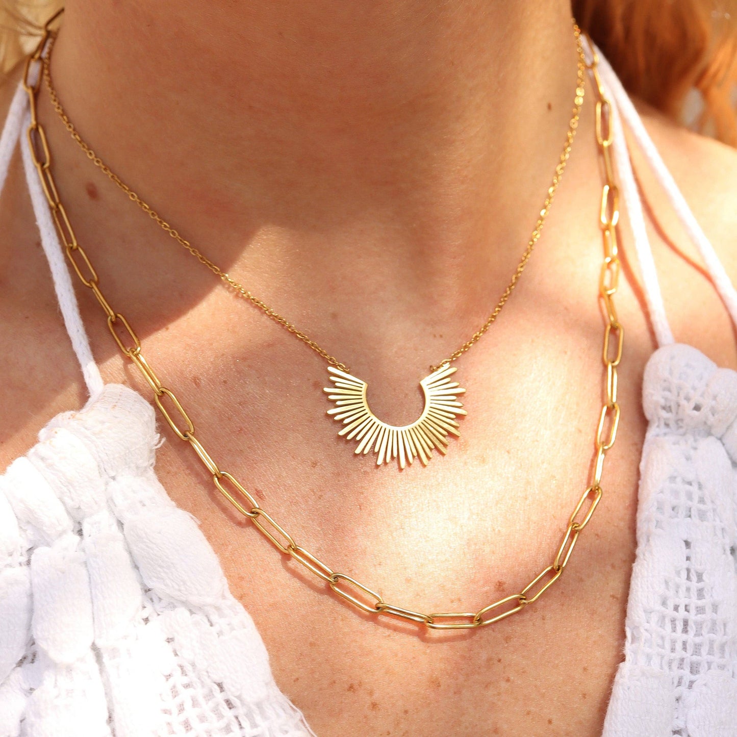 Gold necklace with a sunburst design worn by a person in a white top.